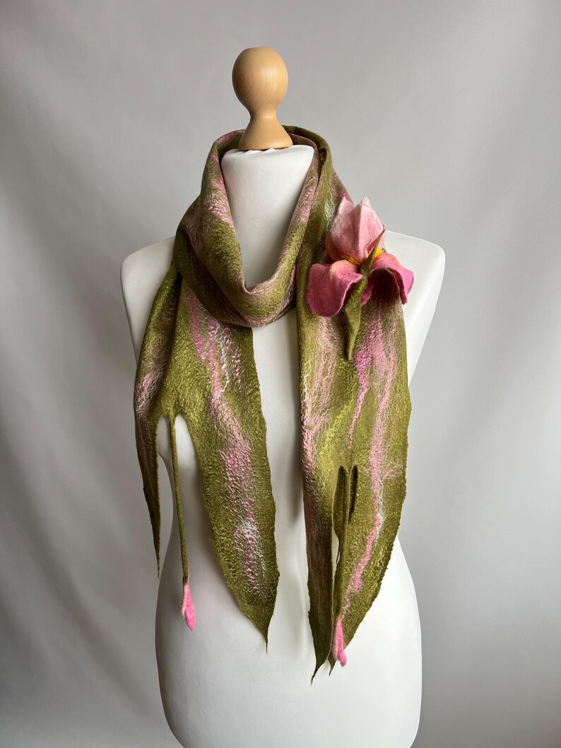 May include: A green and pink felt scarf with a floral accent. The scarf is draped on a mannequin, showcasing a design with vertical stripes of green and pink. A pink felt flower is attached to the scarf, adding a touch of elegance.