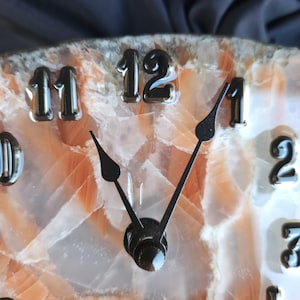 May include: A clock face with black Roman numeral hour markers on a white and orange background. The clock hands are black and point to the 1 and 12.
