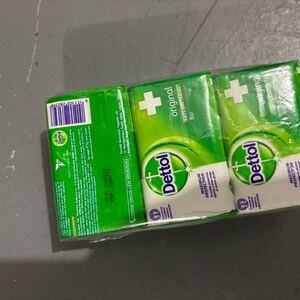 May include: A three-pack of Dettol Original Anti-Bacterial soap bars wrapped in clear plastic. Each green and white bar features the Dettol logo, a white cross, and the text Maximum Protection. The packaging includes a barcode and ingredient list.