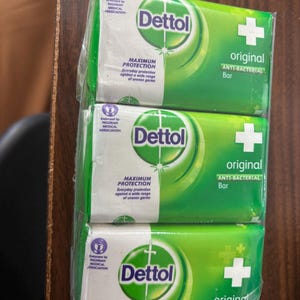 May include: A three-pack of Dettol Original anti-bacterial soap bars wrapped in clear plastic. Each green and white rectangular package features the Dettol logo, a white cross, and the text Maximum Protection, Everyday protection against a wide range of unseen germs.