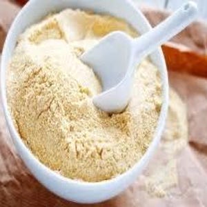 以下が含まれることがあります： 黄色い粉末が入った白いセラミックボウル。おそらく小麦粉または同様のベーキング材料。白いスプーンがボウルの中にあります。ボウルは茶色の紙の表面に置かれ、周りに粉末がこぼれています。