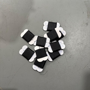 May include: A collection of black thread spools with white paper labels. The spools are arranged on a gray surface. The thread appears to be tightly wound, and the labels are visible.