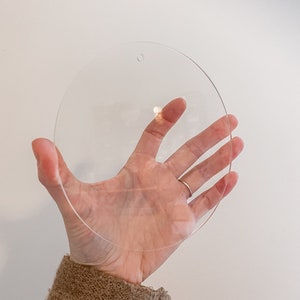 以下が含まれることがあります： 上部に小さな穴が開いた透明な円形の アクリル ディスク。ディスクは手で持たれています。