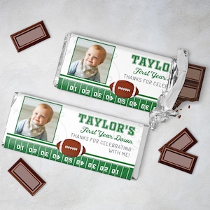 May include: Two green and white chocolate bar wrappers with a football theme. The wrappers feature a photo of a baby boy and the text "TAYLOR'S First Year Down" and "THANKS FOR CELEBRATING WITH ME!"