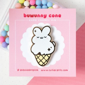 May include: A hard enamel pin featuring a cute bunny-shaped ice cream cone design. The pin has a white ice cream cone with a gold outline and a yellow waffle cone. The pin is on a pink card with the text "buwunny cone".