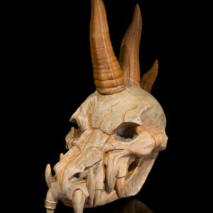 May include: A detailed, beige-colored skull with prominent, upward-curving brown horns. The skull features sharp teeth and intricate detailing, with a textured surface and a dark background. The design suggests a fantasy or gothic theme.