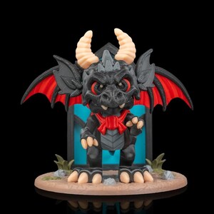 Könnte beinhalten: Eine schwarze Drachenfigur mit roten Flügelakzenten, einer roten Schleife und beigefarbenen Hörnern. Der Drache hat einen strengen Ausdruck und steht auf einer kreisförmigen Basis mit kleinen Pflanzen. Der Hintergrund zeigt eine blaue und schwarze Struktur.