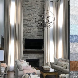 Può includere: Tende beige dal pavimento al soffitto incorniciano un camino in pietra con una televisione montata e un grande lampadario a sfera in metallo nero. Il soggiorno presenta divani dai colori chiari con cuscini decorativi e una striscia di campioni di tessuto a destra.