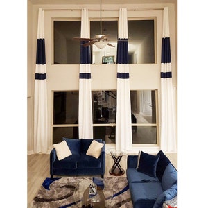 May include: White curtains with navy blue stripes and a matching navy blue sofa set. The room has large windows and a modern design. The curtains are long and hang from the ceiling to the floor.