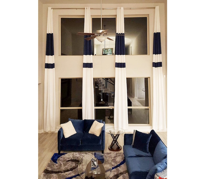 May include: White curtains with navy blue stripes and a matching navy blue sofa set. The room has large windows and a modern design. The curtains are long and hang from the ceiling to the floor.
