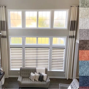 May include: A living room with tall windows and neutral-colored curtains. The curtains are cream-colored with a brown stripe. The windows have blinds. A sofa with pillows is in front of the windows. A color swatch of fabric samples is on the right.