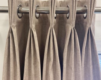 May include: Beige curtains with silver grommets hanging on a silver curtain rod.