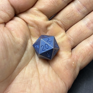 May include: A twenty-sided die with a matte blue finish and dark blue engraved numbers. The die features a prominent number 20 on the top triangular face, with other visible numbers including 14, 8, 6, 16, and 2, arranged in a standard geometric pattern.