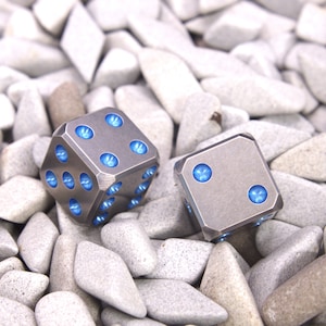 May include: Two silver dice with blue accents, lying on a bed of small gray stones.