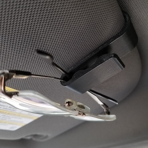 May include: A black plastic car visor clip with a pair of glasses attached to it.