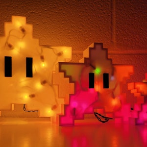 May include: Three pixelated star-shaped light-up figures. The largest is yellow with white lights, the middle is pink with red lights, and the smallest is red with orange lights.