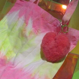May include: A pink and yellow tie-dye tote bag with a pink fuzzy heart keychain attached.