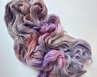 May include: A skein of soft, hand-dyed yarn in shades of lavender, pink, and gray. The yarn is arranged in a loose pile, showing the color transitions.