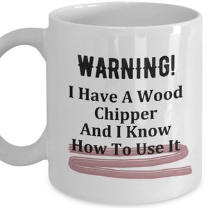 May include: White ceramic coffee mug with a black and white graphic that says "WARNING! I Have A Wood Chipper And I Know How To Use It". The graphic is underlined with a pink line.