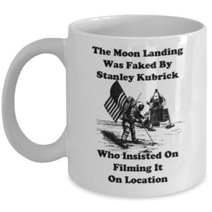 May include: White ceramic mug with a black and white illustration of an astronaut planting a flag on the moon. The text reads "The Moon Landing Was Faked By Stanley Kubrick Who Insisted On Filming It On Location."
