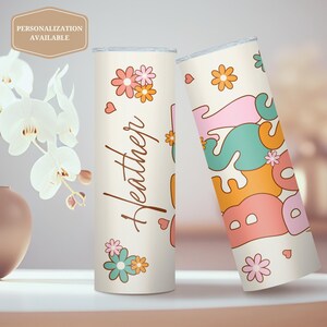 May include: Two personalized stainless steel tumblers with a retro flower and heart design. One tumbler says "Heather" and the other says "Best" in a colorful, retro font.
