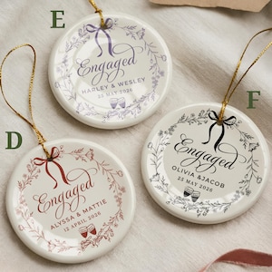 May include: Three white ceramic engagement ornaments with gold string hangers. Each ornament features the word "Engaged" in elegant script, surrounded by floral wreaths and personalized details, including names and dates.