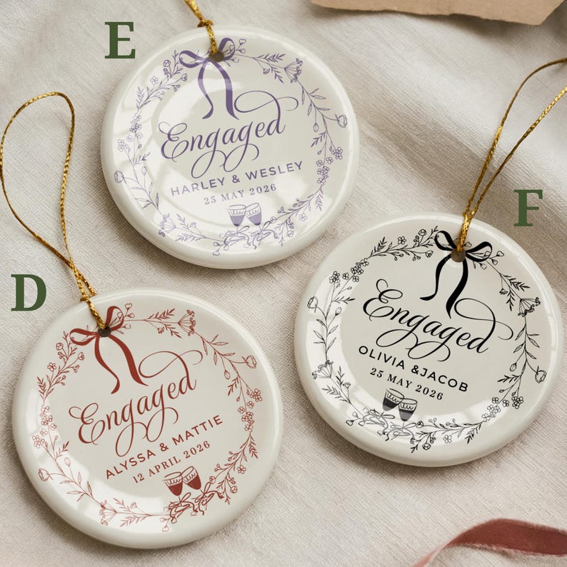 May include: Three white ceramic engagement ornaments with gold string hangers. Each ornament features the word "Engaged" in elegant script, surrounded by floral wreaths and personalized details, including names and dates.