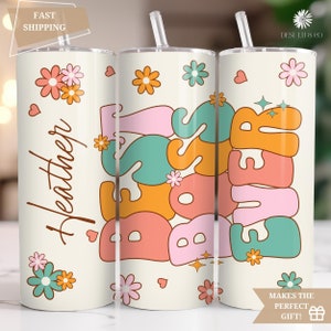 May include: Three white tumblers with lids and straws. The tumblers have a retro design with the words "Boss Babe" and "Forever" in colorful, stylized letters. The tumblers are decorated with flowers and hearts.