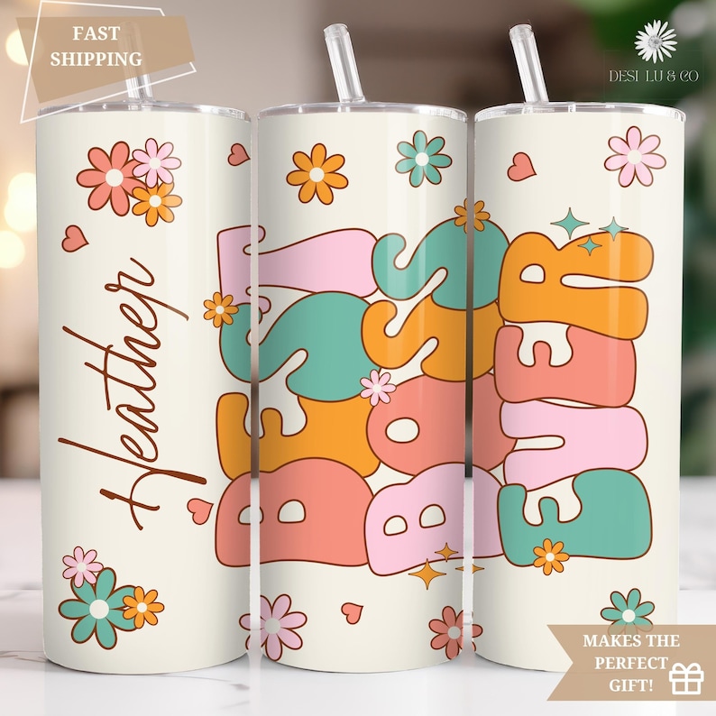 May include: Three white tumblers with lids and straws. The tumblers have a retro design with the words "Boss Babe" and "Forever" in colorful, stylized letters. The tumblers are decorated with flowers and hearts.
