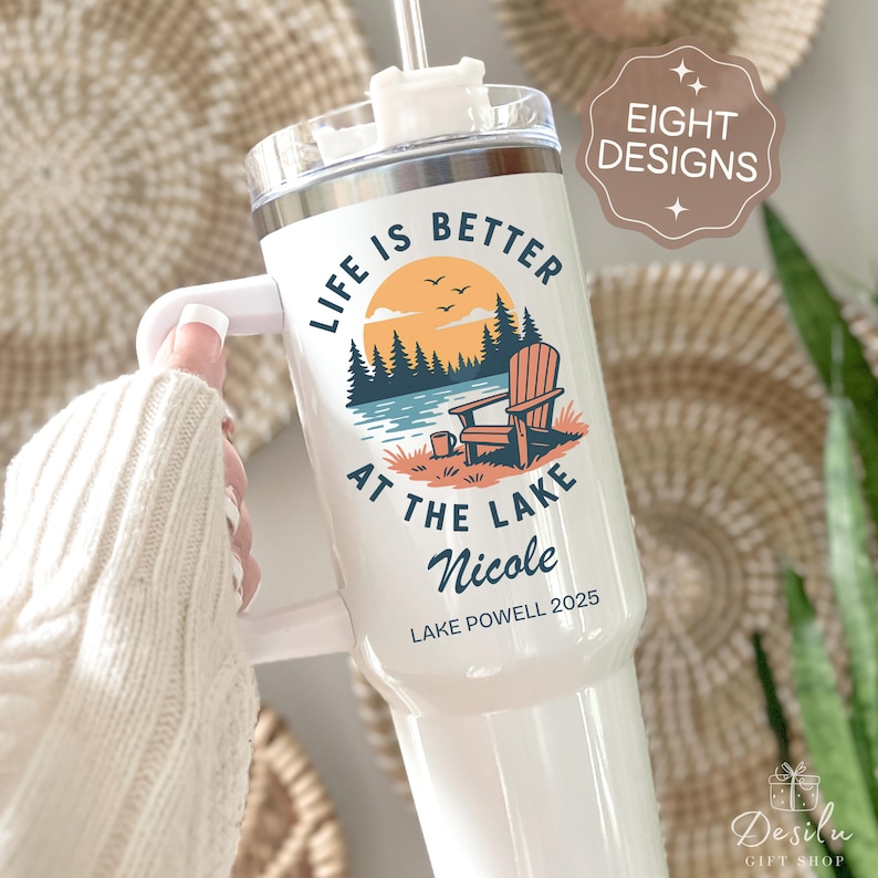 K&ouml;nnte beinhalten: Wei&szlig;er isolierter Becher mit Griff, mit dem Text "Life is Better at the Lake" und einer Szene am Seeufer mit einem Adirondack-Stuhl. Der Becher enth&auml;lt auch den Namen "Nicole" und "Lake Powell 2025".
