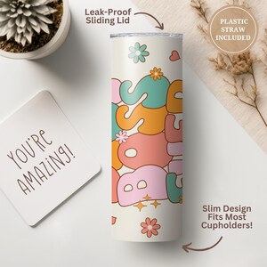 May include: A white stainless steel tumbler with a pastel pink, orange, green, and blue "Boss Babe" graphic. The tumbler has a leak-proof sliding lid and comes with a plastic straw. The tumbler is on a white surface.