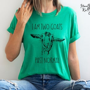 May include: A green t-shirt with a black and white illustration of a goat's face and the text "I am two goats past normal".