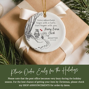 K&ouml;nnte beinhalten: Wei&szlig;er Keramikschmuck mit goldenem Band, mit einer Winnie-the-Pooh-Illustration und dem Text "Some adventures begin with a hello. Ours began with you. Henry Owen Clark ADOPTED 10.14.25". Der Schmuck liegt auf einem Geschenk.