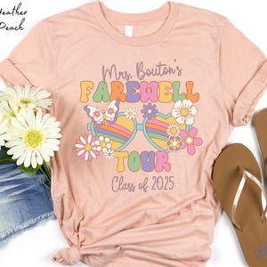 May include: A pink t-shirt with a retro-style design featuring a pair of sunglasses with flowers and the text "Mrs. Bouton's Farewell Tour Class of 2025".