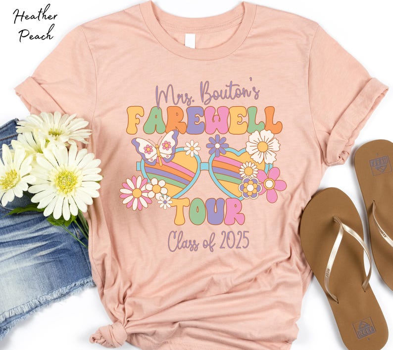 May include: A pink t-shirt with a retro-style design featuring a pair of sunglasses with flowers and the text "Mrs. Bouton's Farewell Tour Class of 2025".