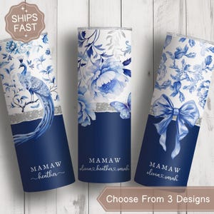 May include: Three stainless steel tumblers with floral designs in blue and white. One features a peacock, another has large flowers, and the third has a bow. Each tumbler has a navy blue base and the word "MAMAW" with names.