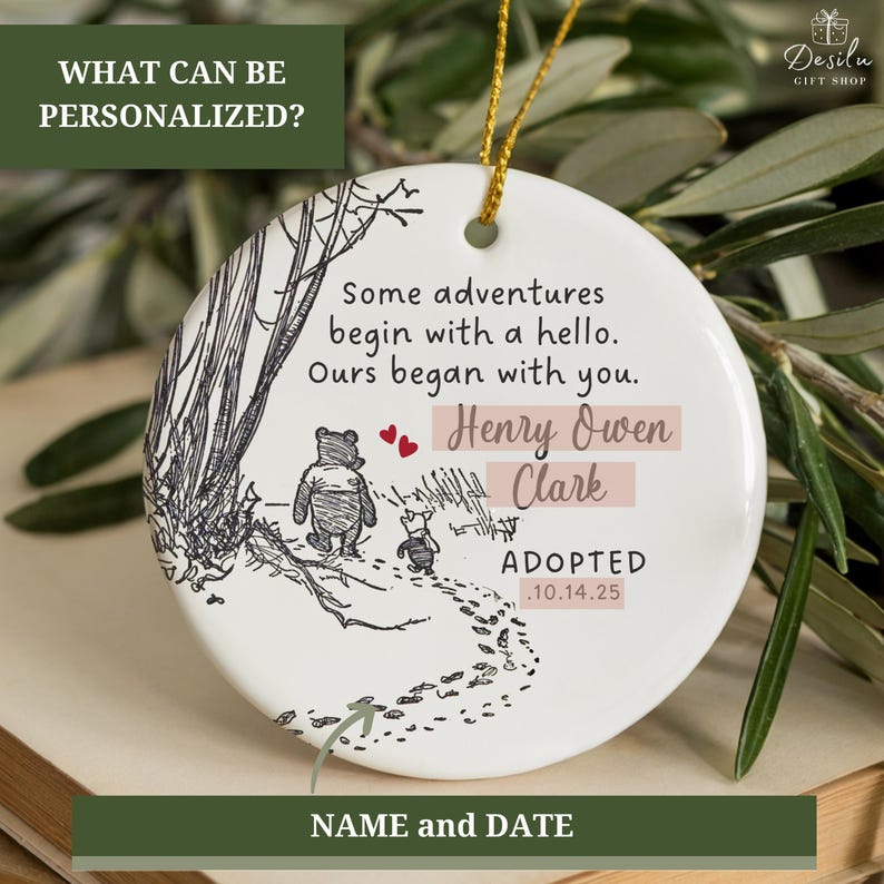 K&ouml;nnte beinhalten: Runder wei&szlig;er Keramikschmuck mit Winnie-the-Pooh-Motiv. Der Schmuck zeigt eine Skizze von Winnie Puuh und Ferkel, die auf einem Pfad gehen. Der Text enth&auml;lt "Some adventures begin with a hello. Ours began with you." und personalisierte Namen und Daten.