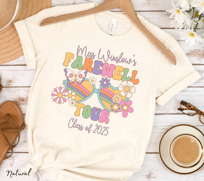 May include: A white t-shirt with a retro-style graphic design featuring a pair of sunglasses with flowers and a butterfly. The text on the shirt reads "Miss Winslow's Farewell Tour Class of 2025".