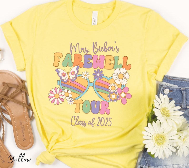 May include: Yellow t-shirt with a retro-style graphic that says "Mrs. Bichen's Farewell Tour Class of 2025". The graphic features a pair of rainbow heart-shaped sunglasses with a butterfly and flowers.