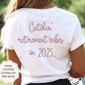 May include: White t-shirt with the text "Catchin' retirement vibes in 2025" printed on the back in pink.