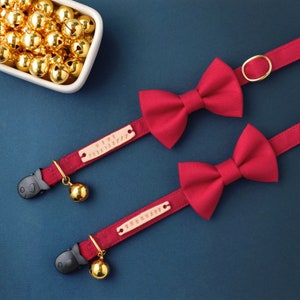 May include: Two red bowtie cat collars with gold bells and personalized name tags. The name tags read "HIMI 026158777" and "THORNADO".