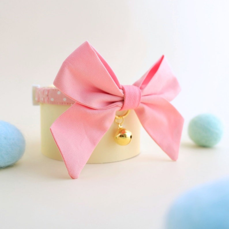 May include: Pink bow with a gold bell attached to a white collar with white polka dots.