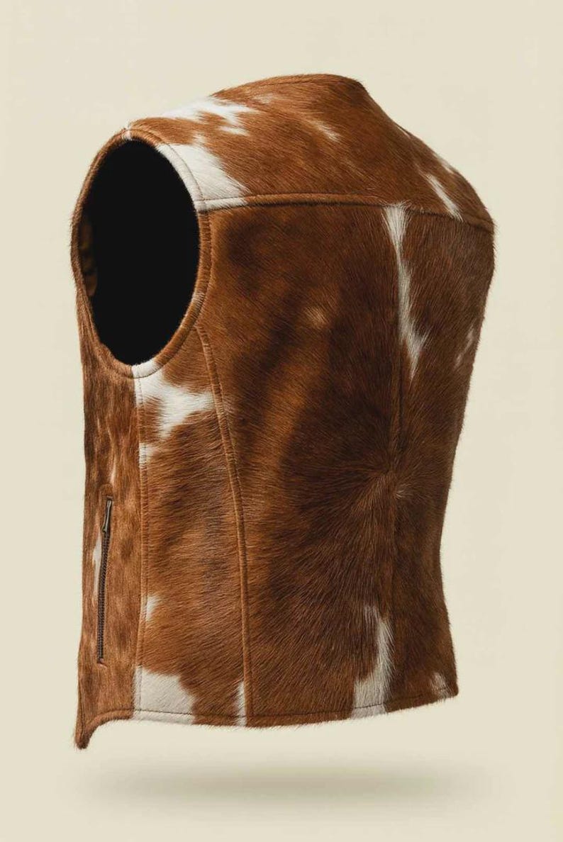 May include: A brown and white cowhide vest with a zipper closure. The vest has a round neckline and a tailored fit. The natural pattern of the cowhide is visible, with brown and white patches. The vest is a unique piece of outerwear.