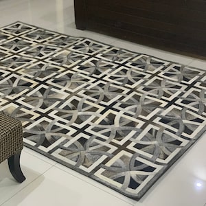 Può includere: Tappeto rettangolare con motivo geometrico nei toni del grigio, nero e bianco. Il design del tappeto presenta forme ripetute e interconnesse, creando un aspetto moderno. Il tappeto sembra essere realizzato in un materiale morbido.