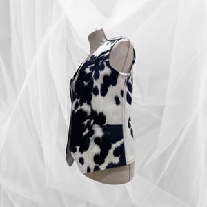 May include: A sleeveless vest with a black and white cow print pattern. The vest has a zipper closure and a pointed collar.