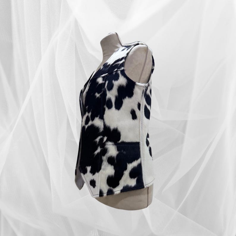 May include: A sleeveless vest with a black and white cow print pattern. The vest has a zipper closure and a pointed collar.