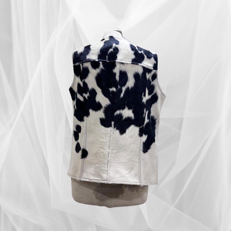 May include: A sleeveless vest with a black and white cow print pattern. The vest is made of a soft, textured material.