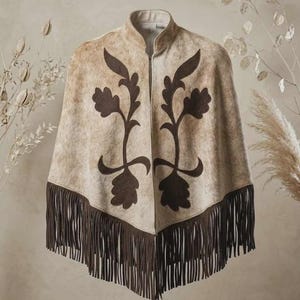 May include: A beige and tan textured poncho featuring a high collar and a front zipper closure. The garment is decorated with dark brown symmetrical floral applique patterns on the front and finished with a long dark brown fringe hemline.