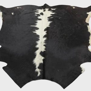 Può includere: Un tappeto in pelle di mucca con un sorprendente motivo bianco e nero. Il tappeto presenta una base prevalentemente nera con una striscia bianca centrale e accenti bianchi lungo i bordi. La forma naturale della pelle è visibile.
