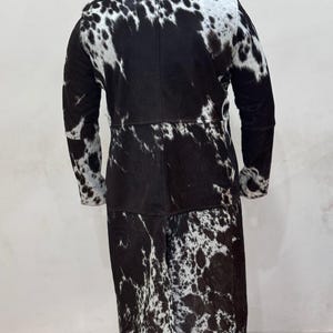 Puede incluir: Un abrigo largo de piel de vaca negro y blanco con manga larga y cuello.